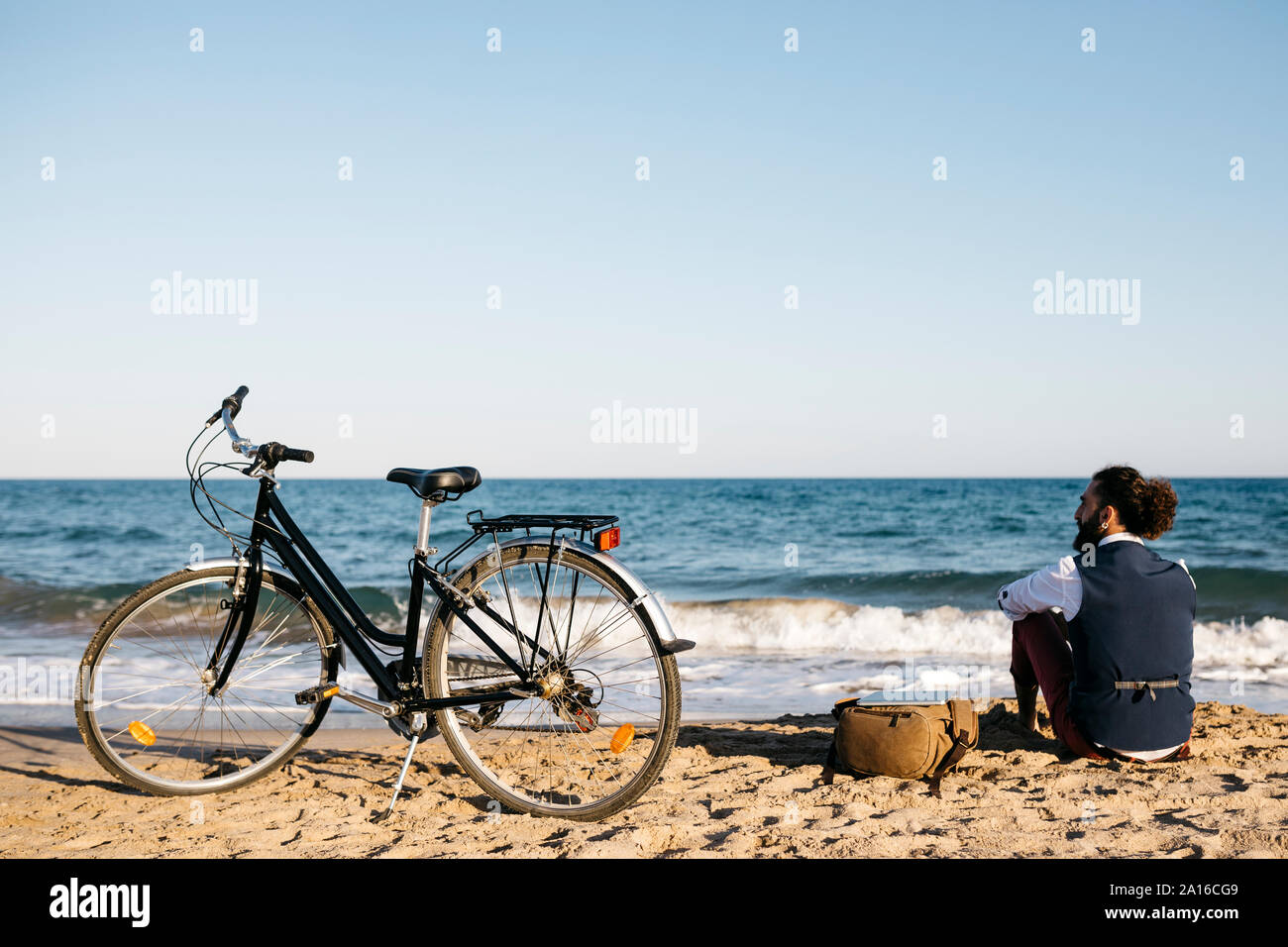 Gut gekleideter Mann mit seinem Fahrrad sitzen auf einem Strand Stockfoto