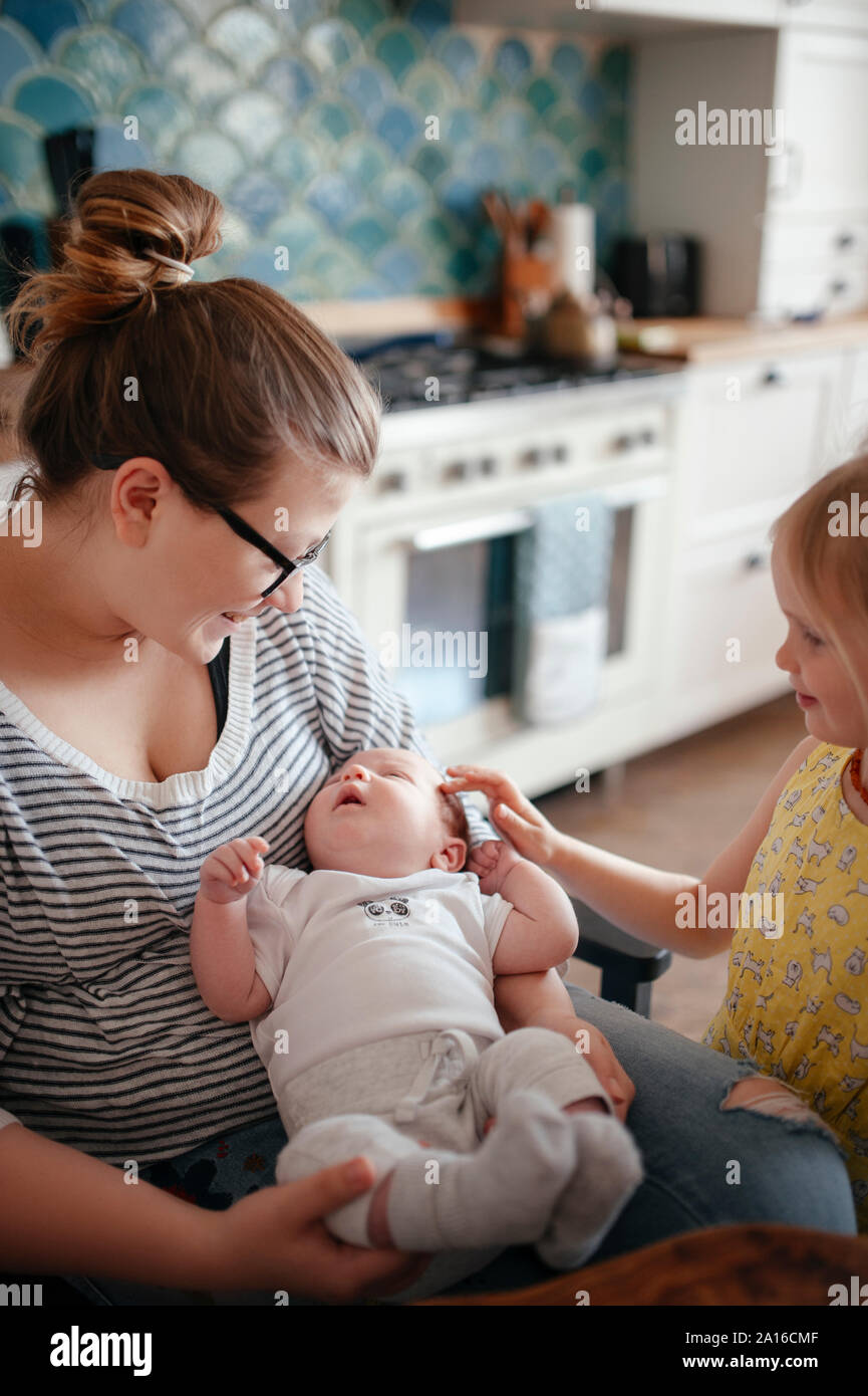 Lächelnde Frau mit ihrem Baby und die ältere Tochter in der Küche Stockfoto