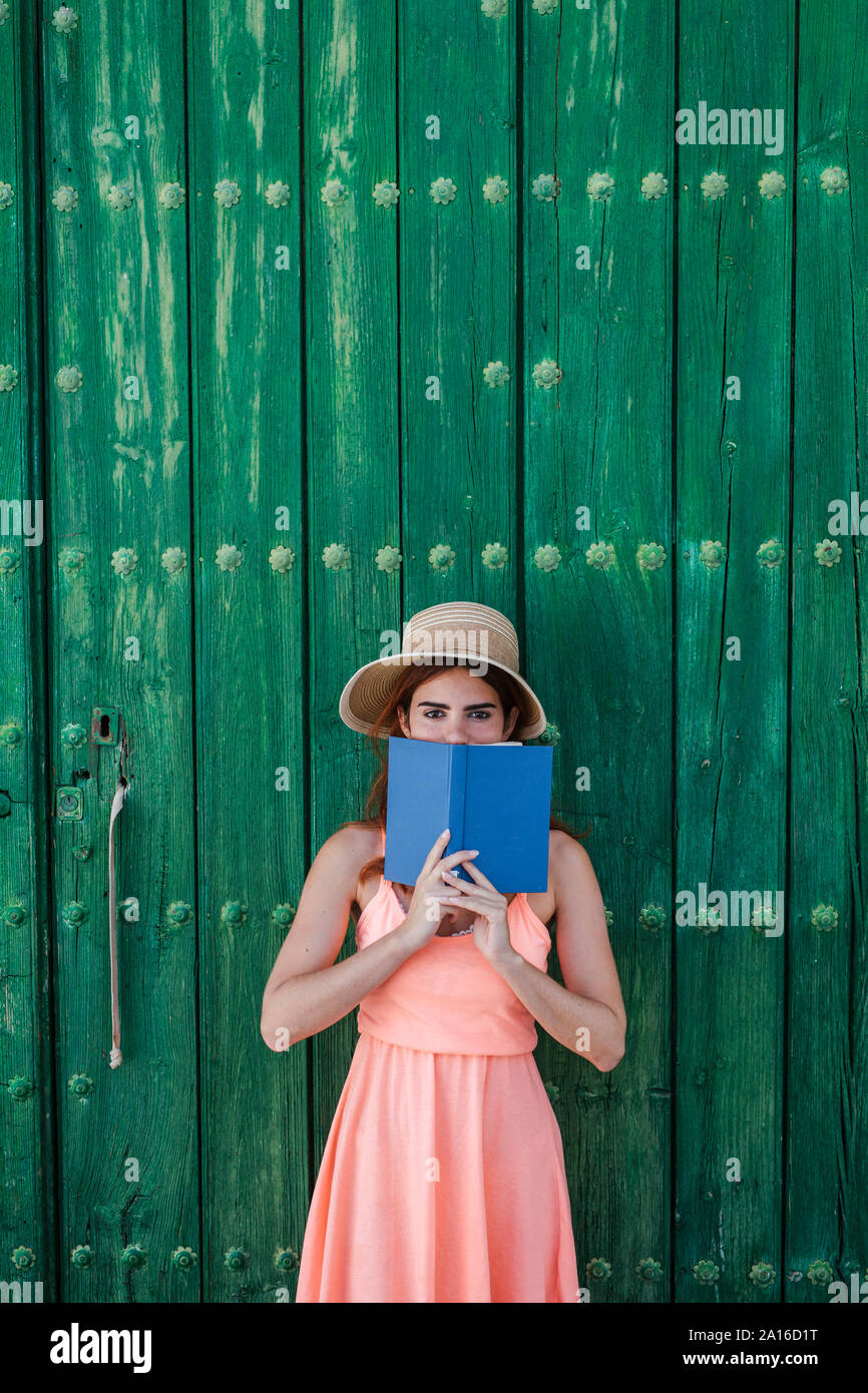 Porträt der jungen Frau stand vor der grünen Holztür mit einem Buch im Sommer Stockfoto