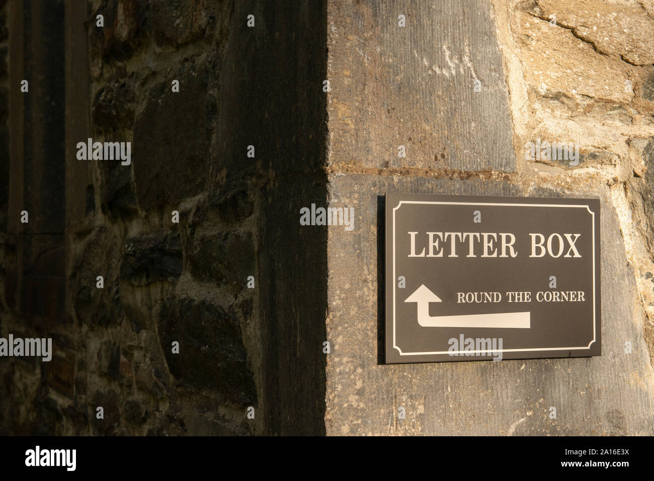Briefkasten um die Ecktafel mit einer Pfeilmarkierung, die in die Richtung zeigt und an einer Steinwand des Gebäudes angebracht ist Stockfoto