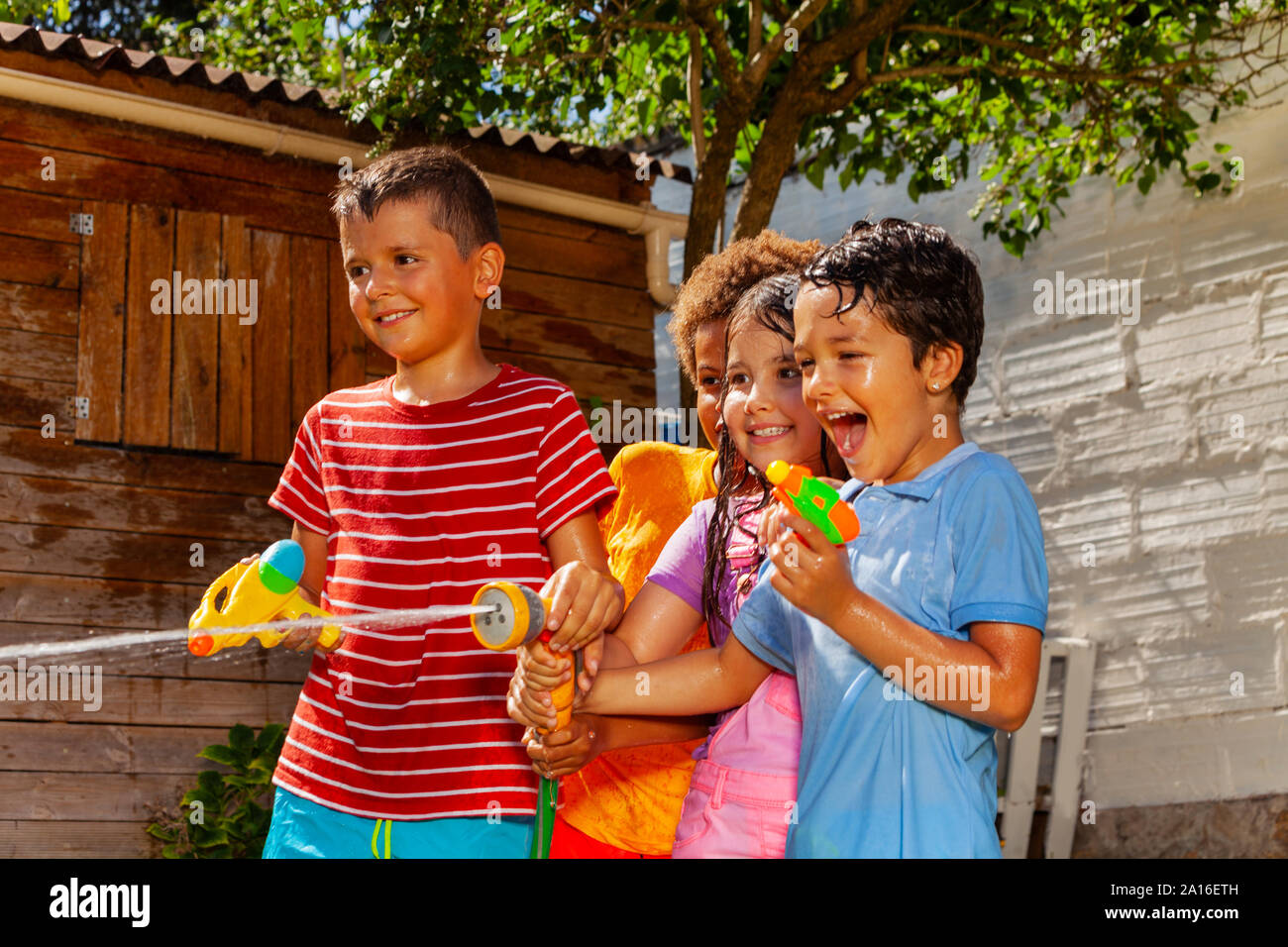 Lächelnd und sprechen Kinder schiessen mit Wasserkanonen nass vom Spiel zusammen Jungen, Mädchen Stockfoto