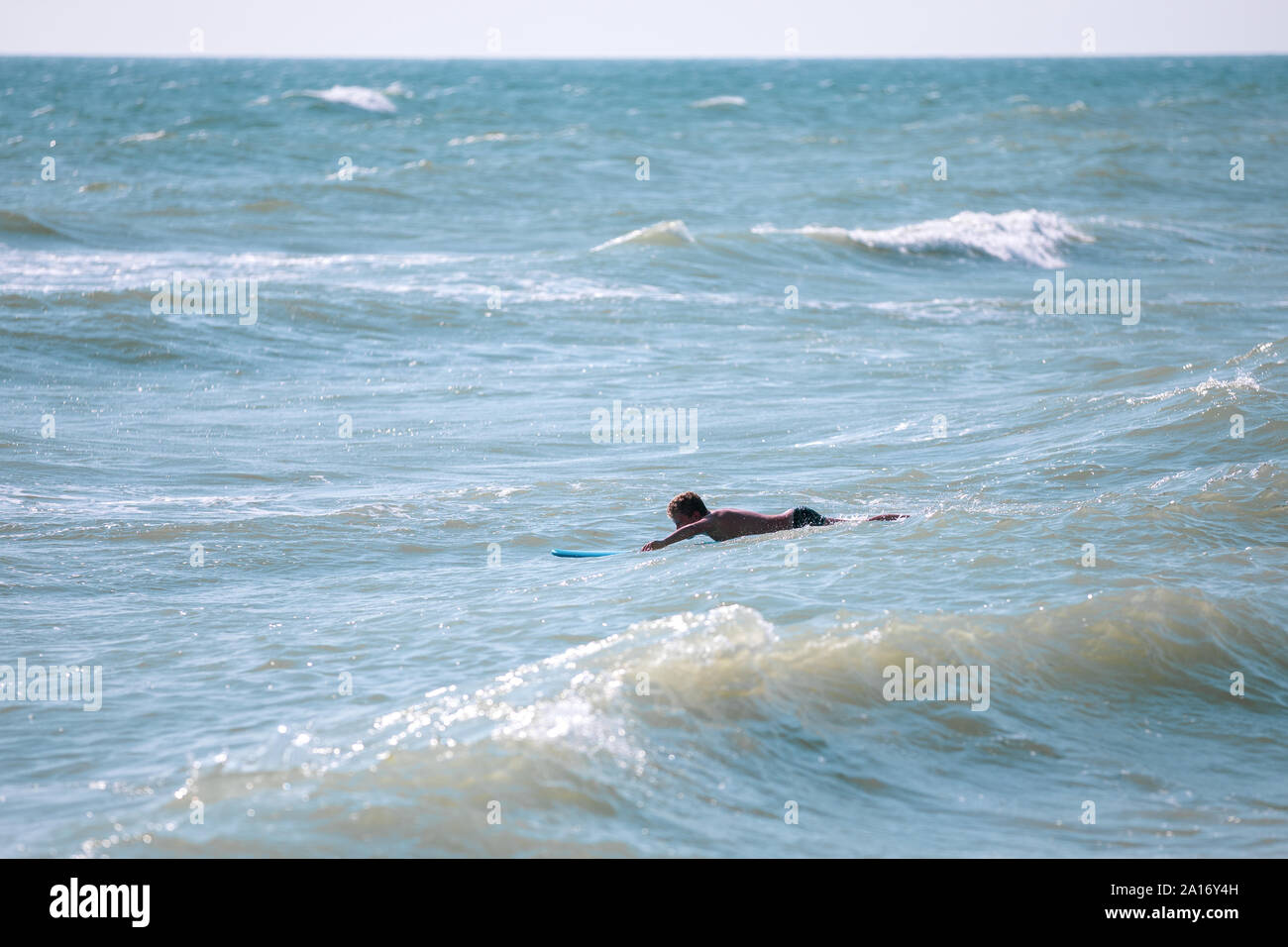 Mann mit Surfbrett im Meer schwimmen Stockfoto