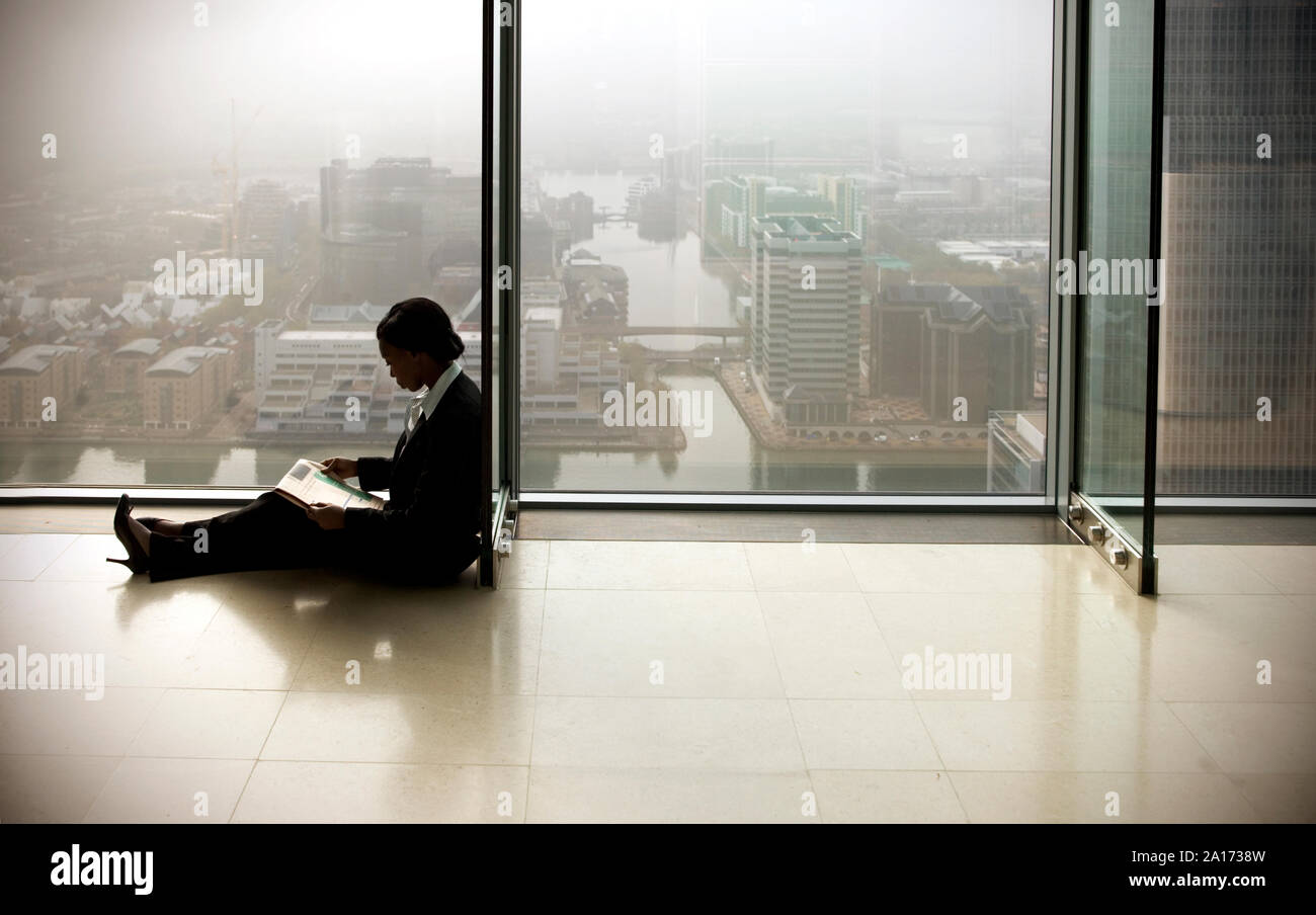 Junge Geschäftsfrau, sitzen auf dem Boden, während Sie die Zeitung lesen. Stockfoto