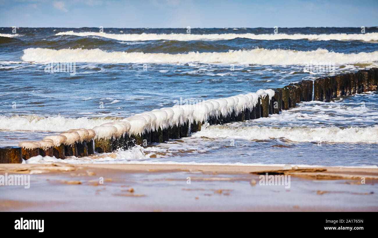 Strand mit einem eisigen Holz- wellenbrecher an einem sonnigen Tag. Stockfoto