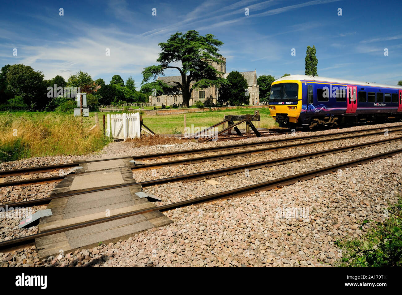 Eine erste große westliche Zug auf einem Abstellgleis vor der Kirche St. Mary, Great Bedwyn, Wiltshire. vom Gateway an einem öffentlichen Fußweg Kreuzung gesehen. Stockfoto