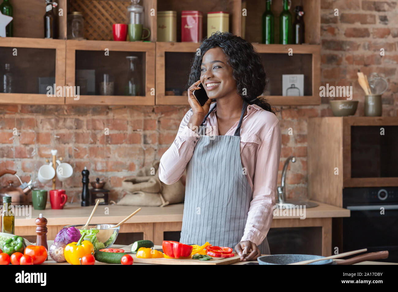 Junge Frau mit angenehmen Gespräch am Telefon, beim Kochen Stockfoto