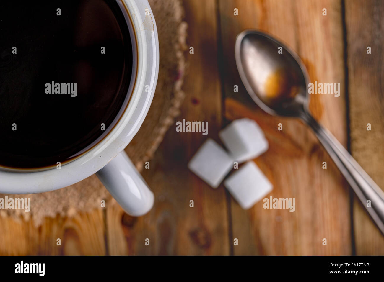 Schwarzen Kaffee in einem grauen Tasse und einem Teelöffel auf einen hölzernen Tisch. Lecker trinken und Weißzucker, stimulierende Wirkung. Der dunkle Hintergrund. Stockfoto