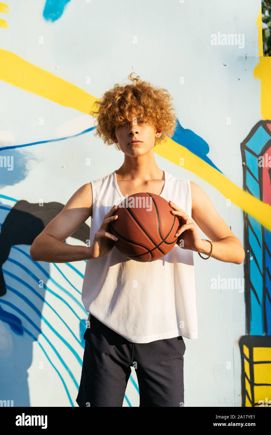 Junge Männer mit kurvigen Haare holding Basketball Ball vor Graffiti Stockfoto