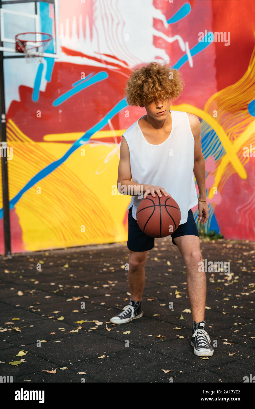 Junge Männer mit kurvigen Haar Basketball spielen draußen im Hof Stockfoto