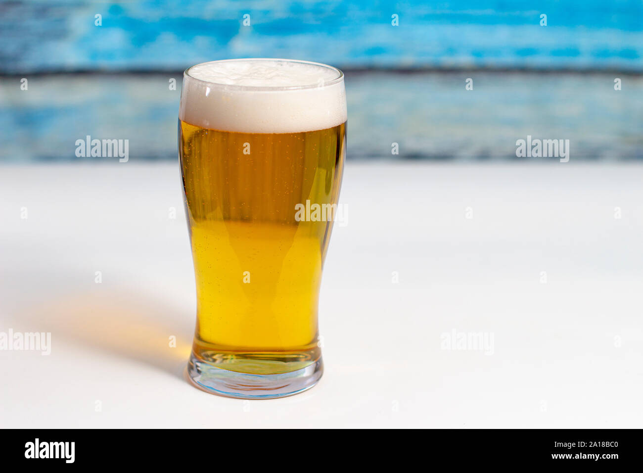 Pint Bier auf einem weißen Tisch mit einem bunten hölzernen Wand Stockfoto