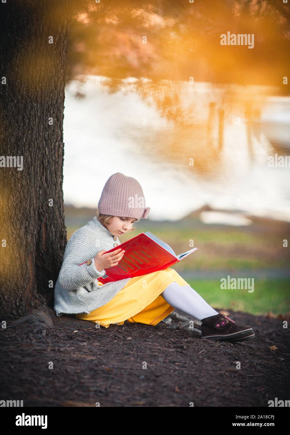 Wenig kaukasische Mädchen ist, das Buch zu lesen, unter dem Baum Stockfoto