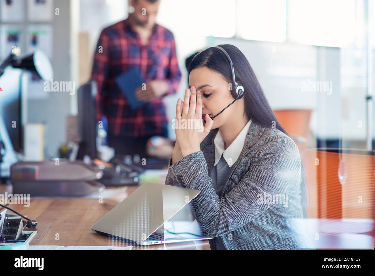 Müde junge Frau sitzt am Tisch bei der Arbeit in einem Call Center. Stockfoto