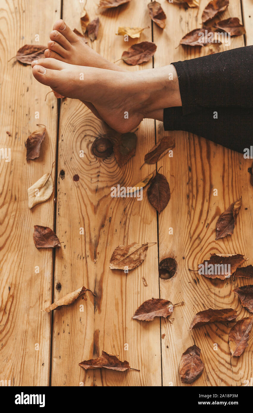 Die Füße der Person auf dem Holzboden mit Herbstlaub bedeckt. Herbst Konzept mit kopieren. Holzhaus, entspannen im warmen Herbst Stockfoto