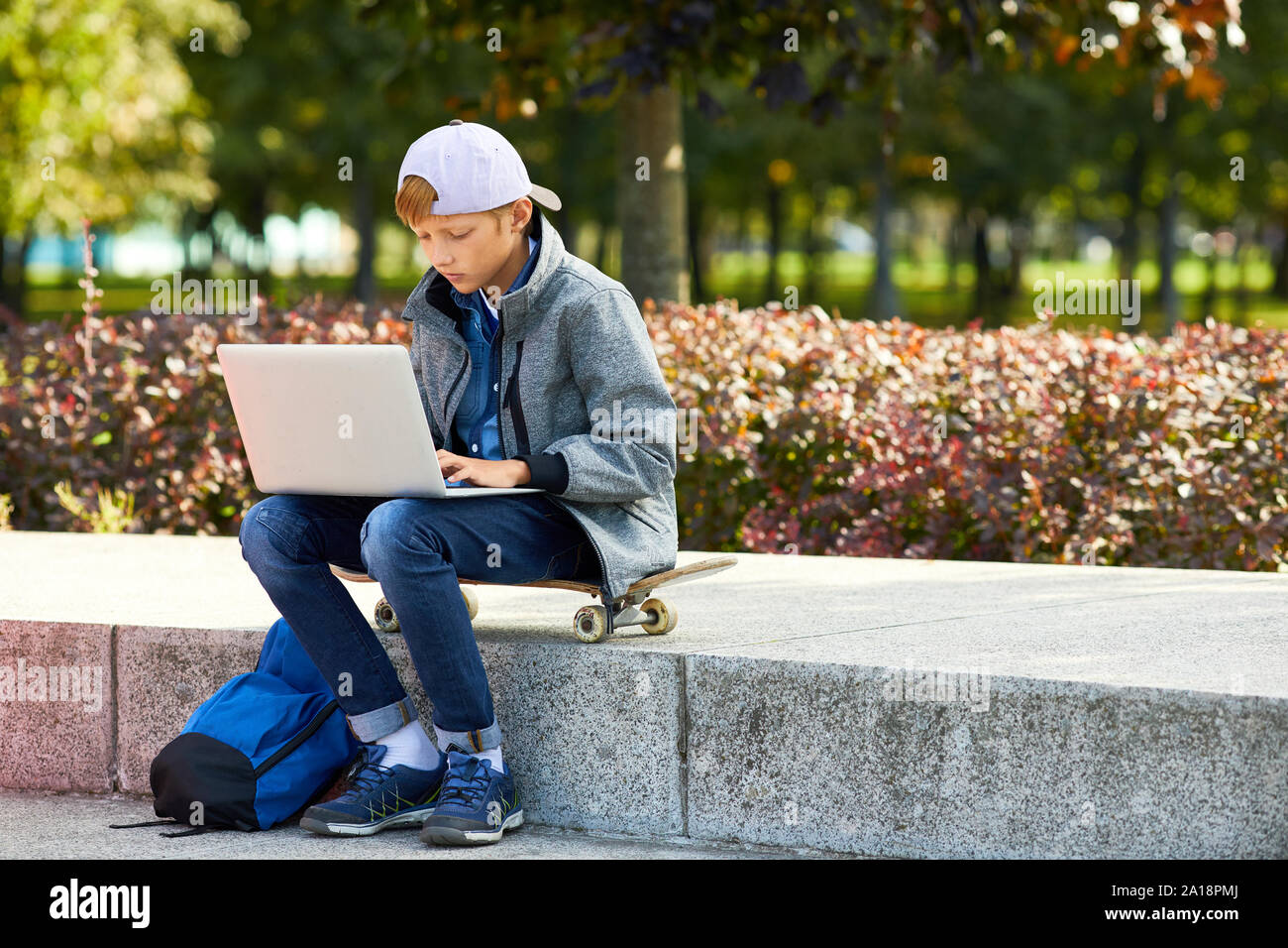 Junge in Freizeitkleidung auf Skateboard und Tippen auf Laptop im Freien er die Vorbereitung für die Hausaufgaben Stockfoto