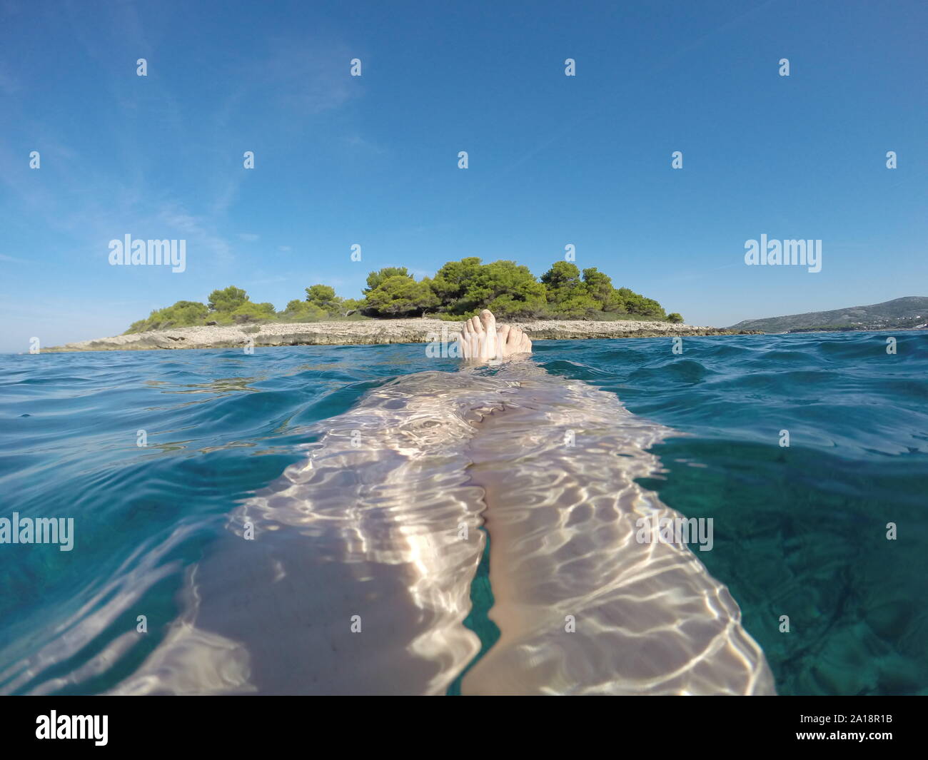 Closeup schoss der Beine der Frau unter dem Meer mit kleinen Insel am Horizont Stockfoto