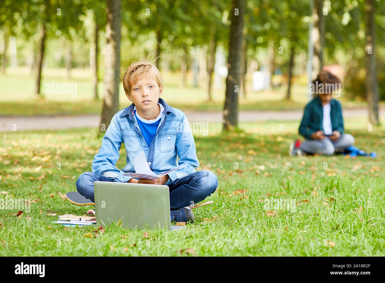 Portrait von Jungen in Freizeitkleidung auf grünem Gras sitzt mit Laptop und Kamera Stockfoto