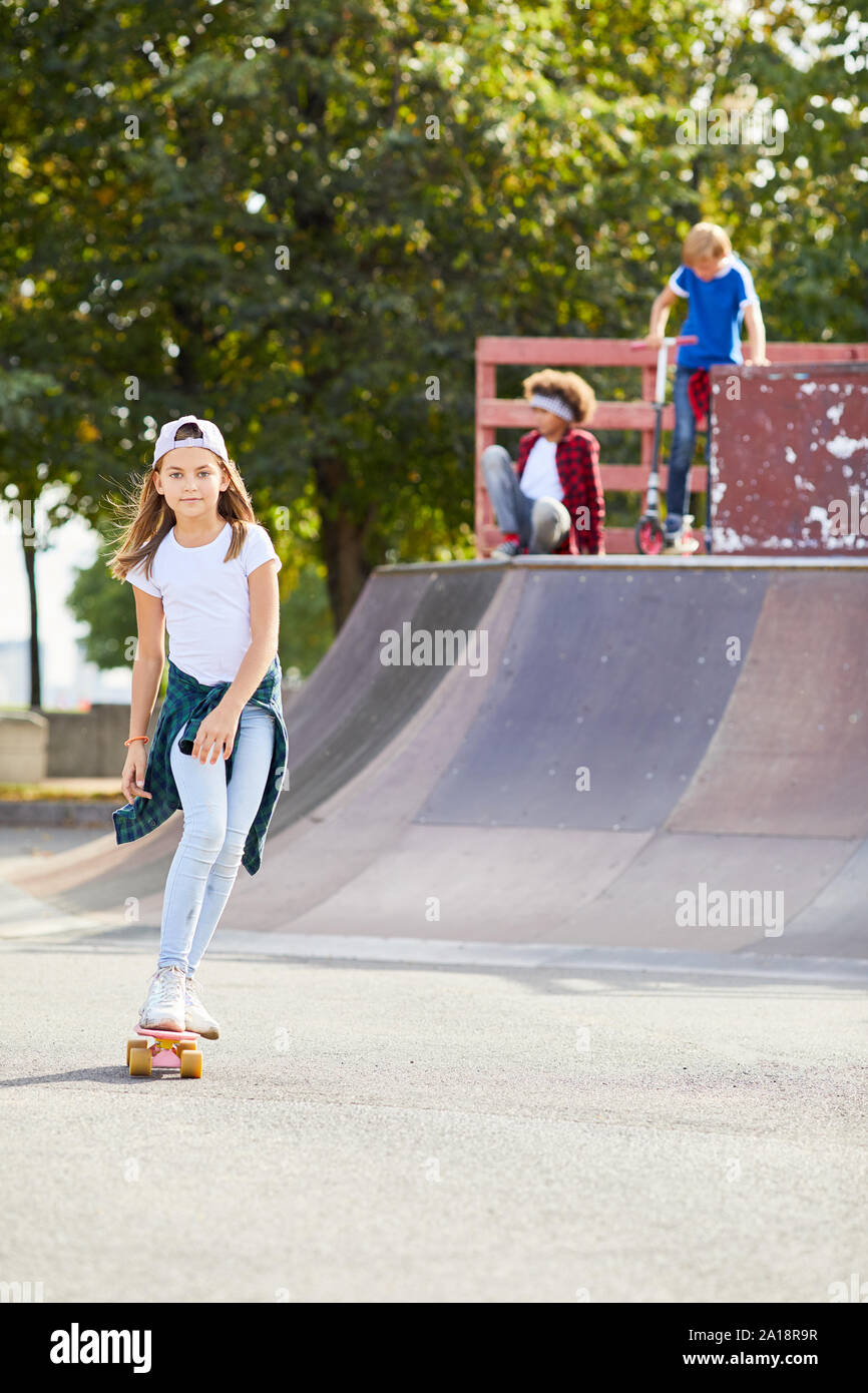 Portrait von cute girl in Freizeitkleidung reiten auf Skateboard mit ihren Freunden bei skateboard Park Stockfoto