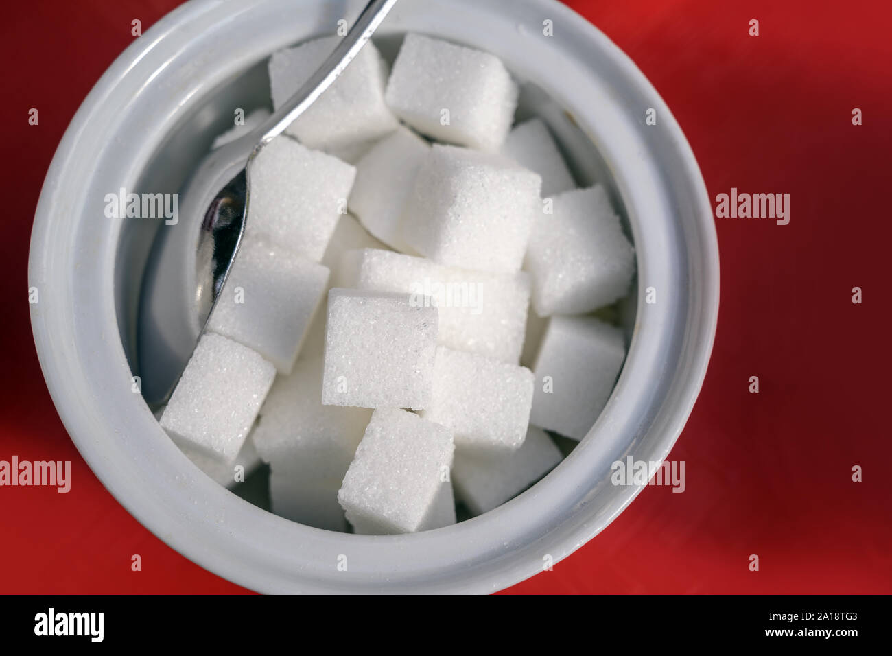 Würfelzucker und Löffel in einer weißen Schüssel auf einem roten Hintergrund, hohen Winkel, Ansicht von oben, ausgewählte konzentrieren, enge Tiefenschärfe Stockfoto
