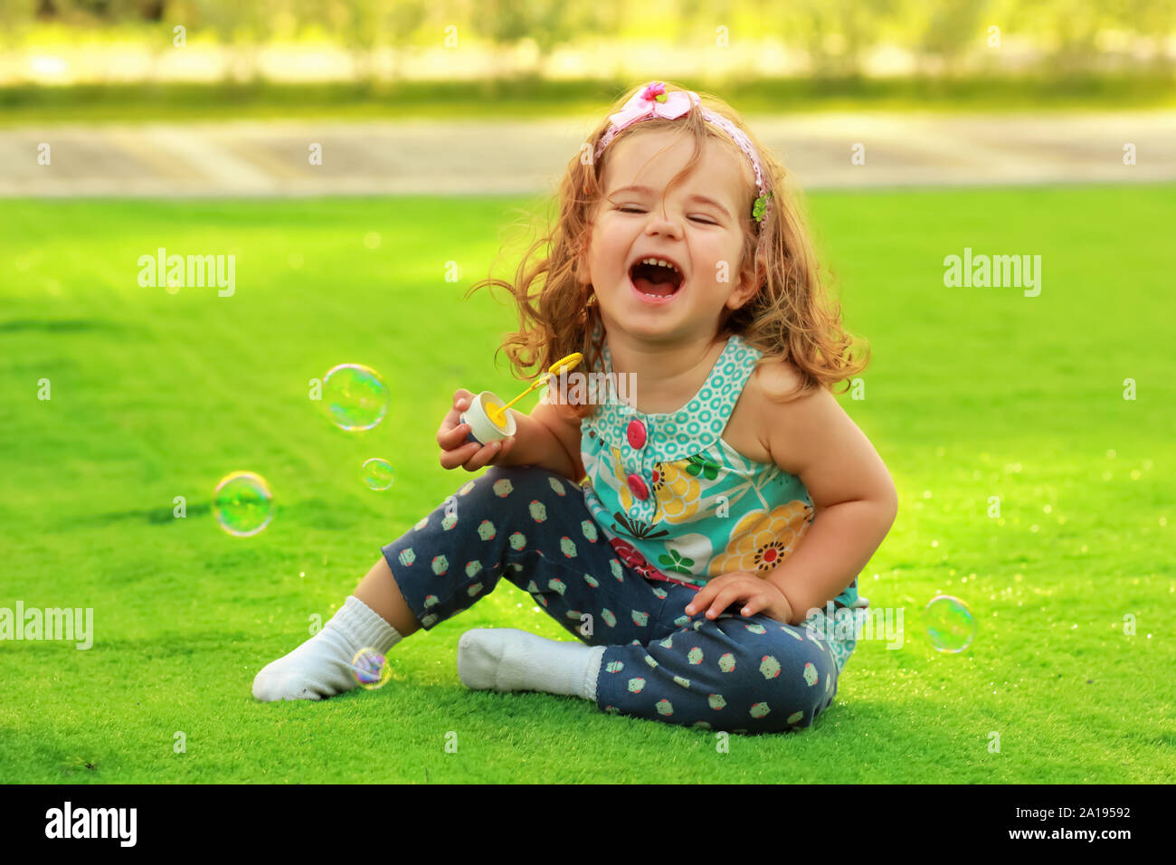 Lachend ein Jahr altes Mädchen lernen Seifenblasen in die Luft zu sprengen und Spaß auf der sonnigen Liegewiese Stockfoto