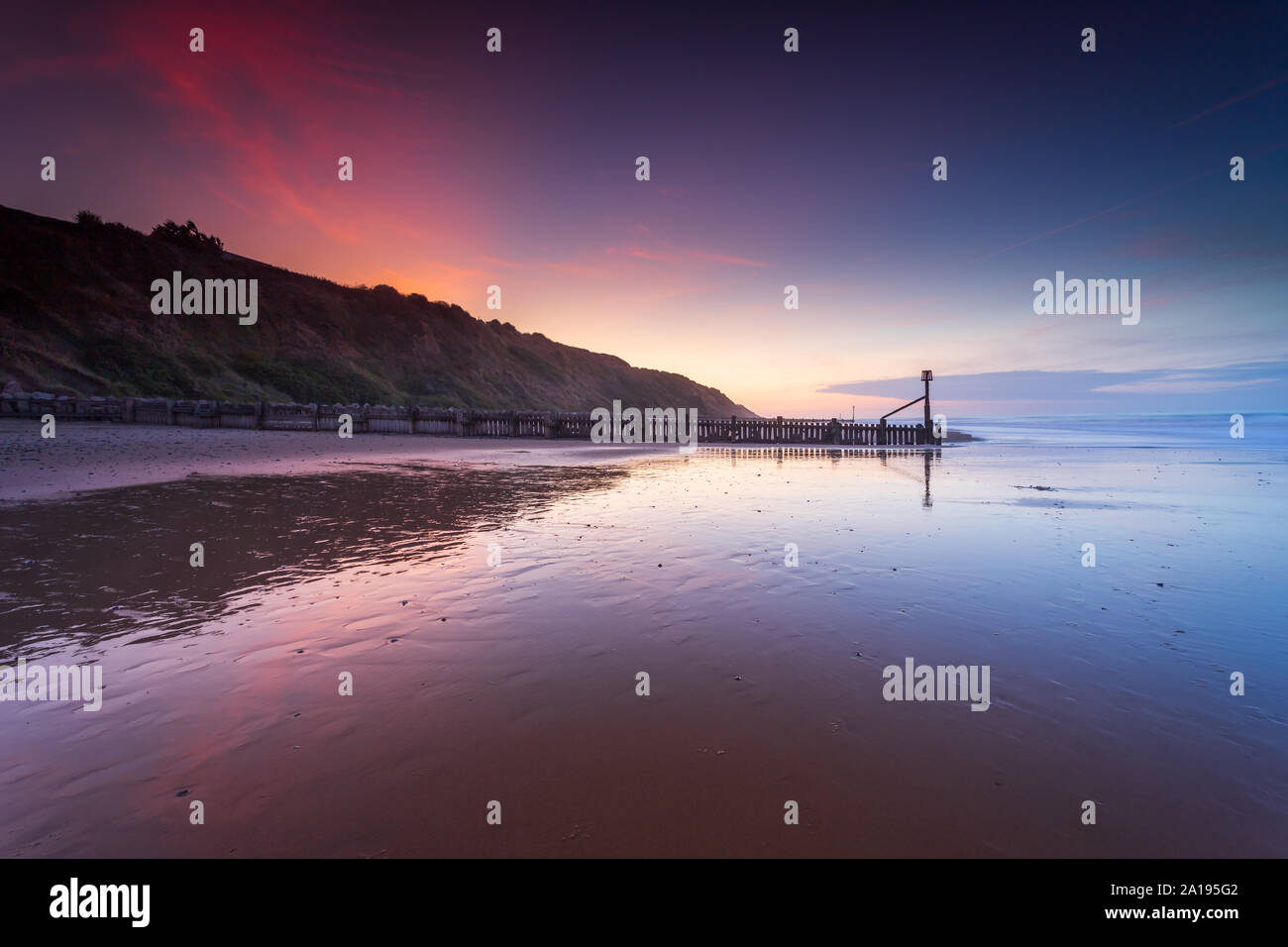 Sonnenuntergang Reflexionen von den Klippen und Buhnen auf der schönen Mundesley Strand in North Norfolk, UK auf einen angenehmen Abend im September 2019 Stockfoto