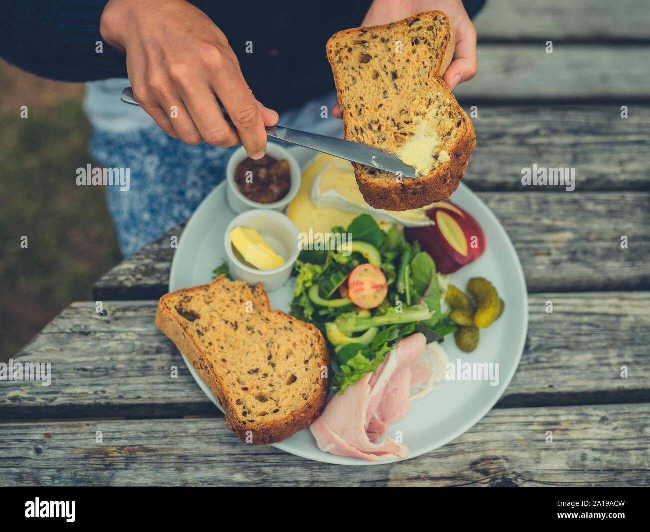 Eine junge Frau wird zustimmen Brot im Freien an einem Picknicktisch ein Sandwich zu machen Stockfoto