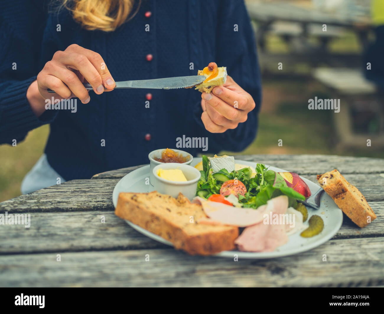 Eine junge Frau wird zustimmen Brot im Freien an einem Picknicktisch ein Sandwich zu machen Stockfoto