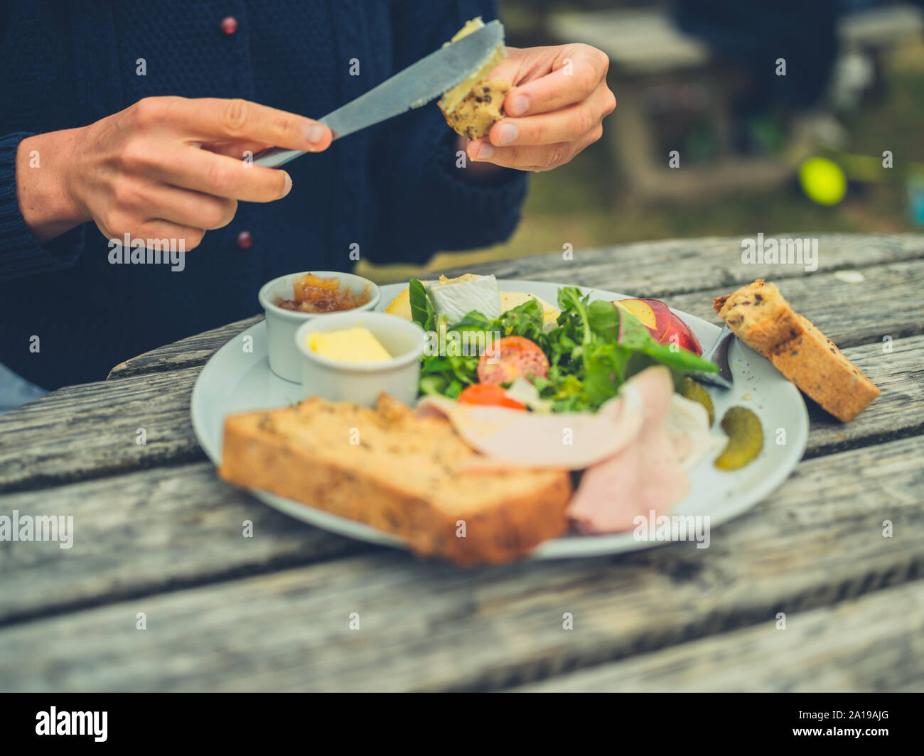 Eine junge Frau wird zustimmen Brot im Freien an einem Picknicktisch ein Sandwich zu machen Stockfoto