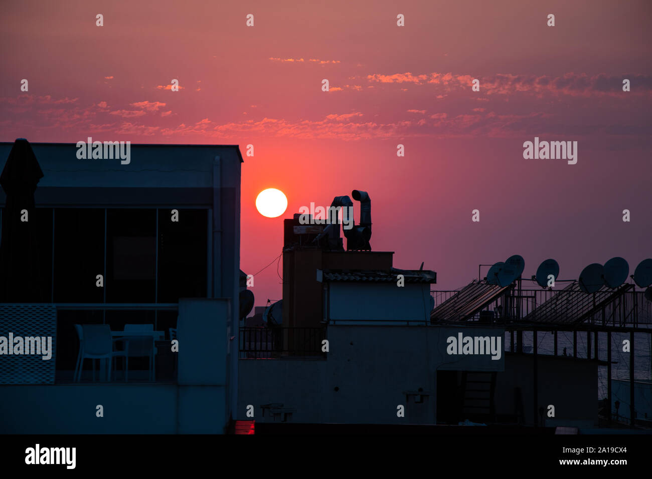 Die Sonne hinter den Dächern der Gebäude, der Himmel violett. Stockfoto