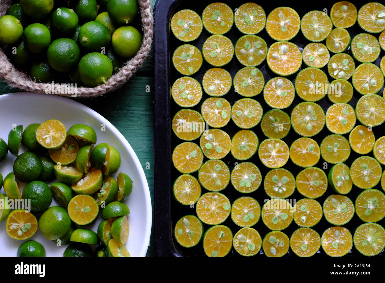 Ansicht von oben schwarz Fach vieler kumquat Obst in der Hälfte mit Green Peel und gelbe Fleisch schnitt am grünen Holz- Hintergrund, dieses saure Früchte reich an Vitamin C, er Stockfoto