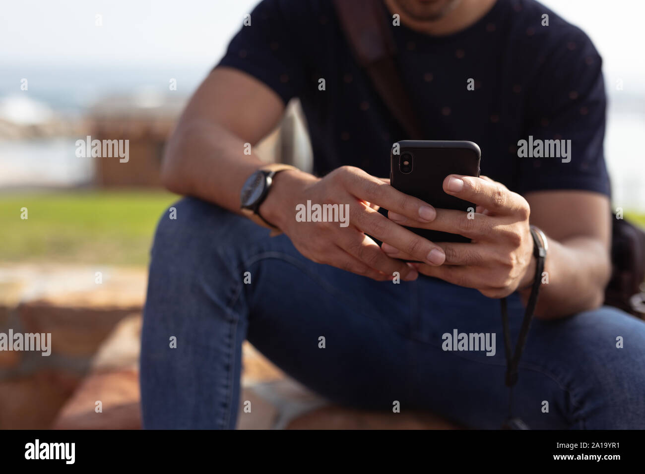 Junger Mann draußen sitzen an einer Wand mit einem Smartphone Stockfoto