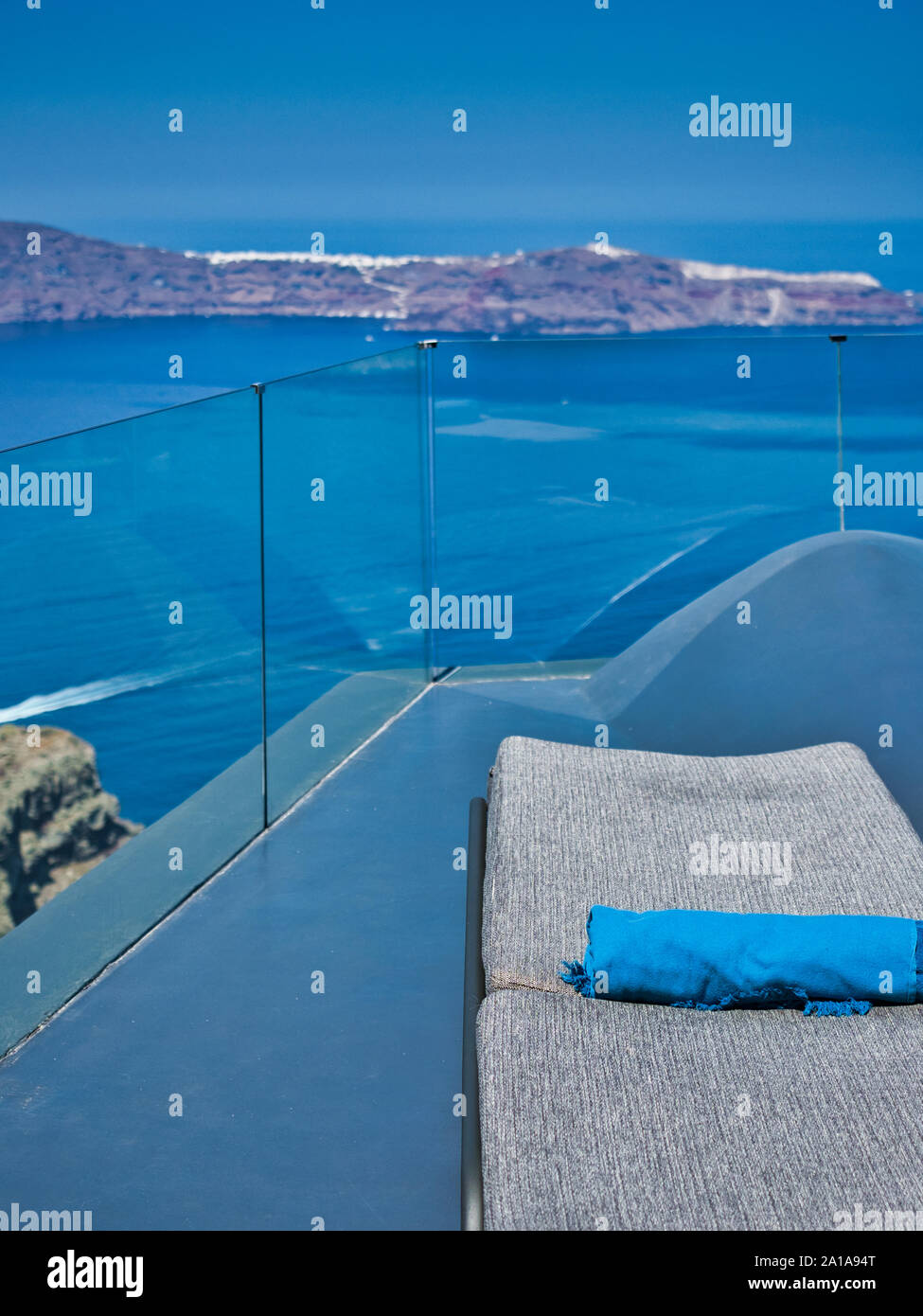 Abgewickelte Chaiselongue mit gerollten Decke auf Balkon über dem blauen Meer und hohen Felsen mit weißen Stadt an einem sonnigen Tag Stockfoto