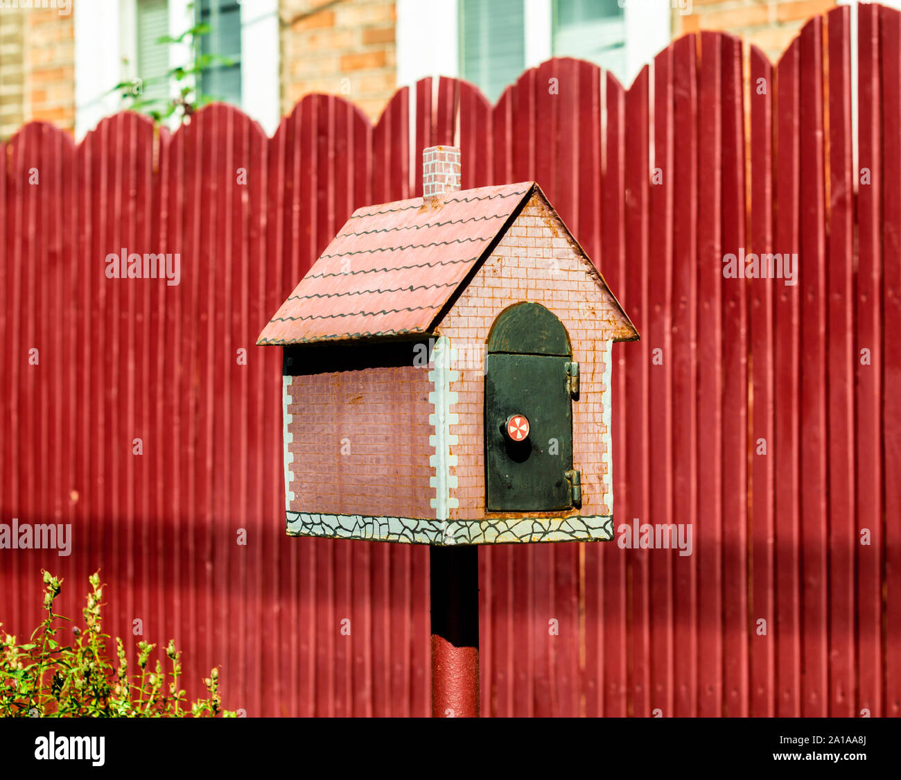 Mailbox in Form von einem kleinen Haus auf dem Hintergrund einer roten Zaun Stockfoto
