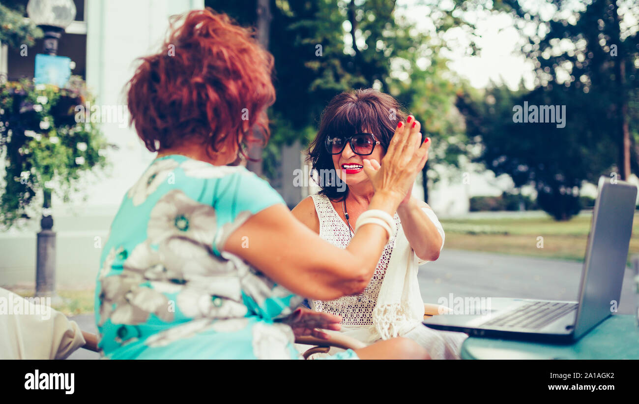 Gerne ältere weibliche Freunde geben High Five, Erfolg feiern, während Sie einander sitzen, die in der Tabelle in einem Café im Freien. Stockfoto