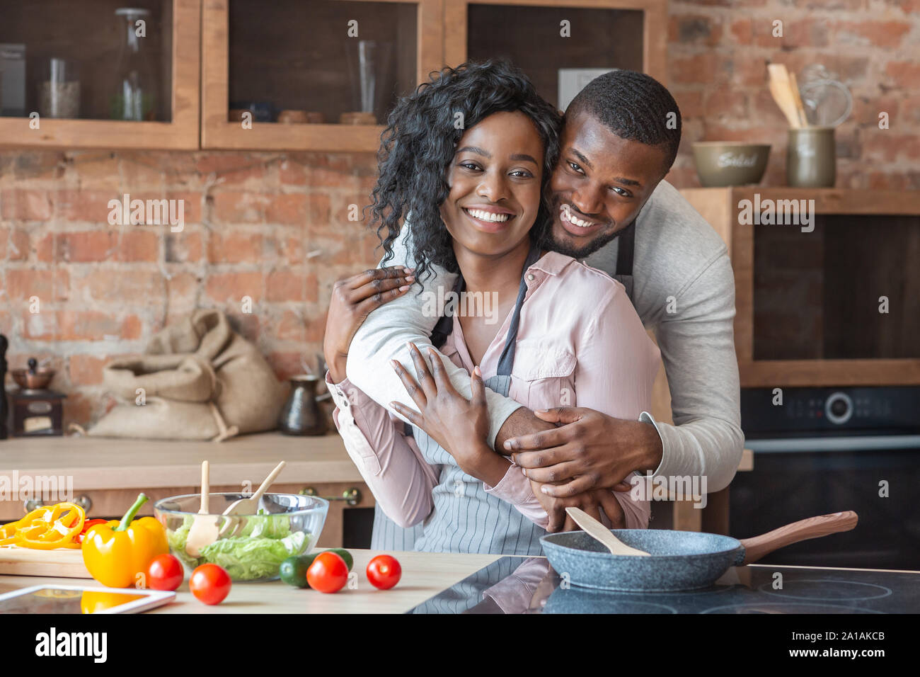 Dankbar afrikanischer Mann umarmt seine Frau beim Kochen in der Küche Stockfoto