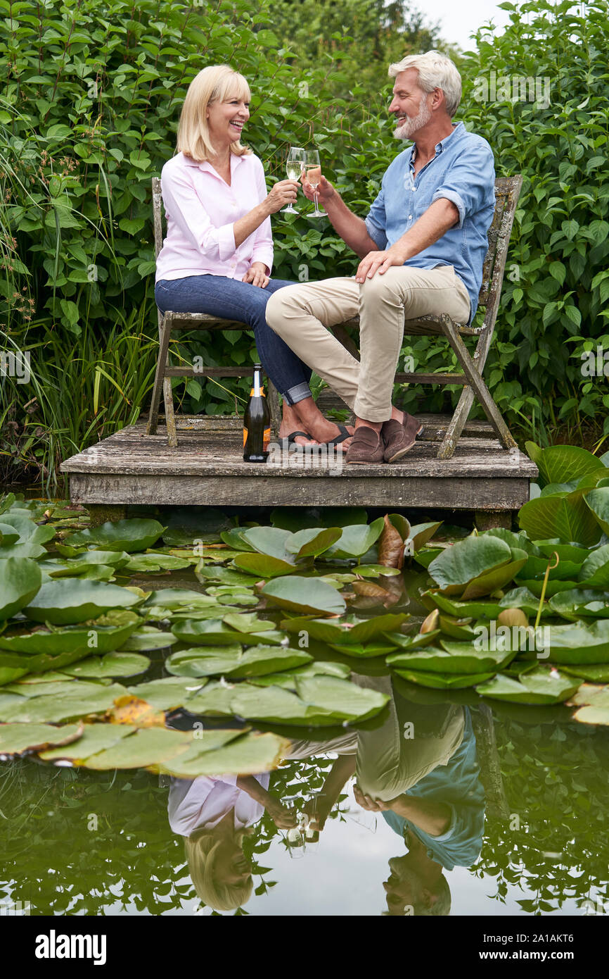 Reifes Paar feiern mit Champagner Sitzen auf Stühlen auf hölzernen Steg am See Stockfoto Reifes Paar feiern mit Champagner Sitzen auf Stühlen auf hölzernen Steg am See Stockfoto