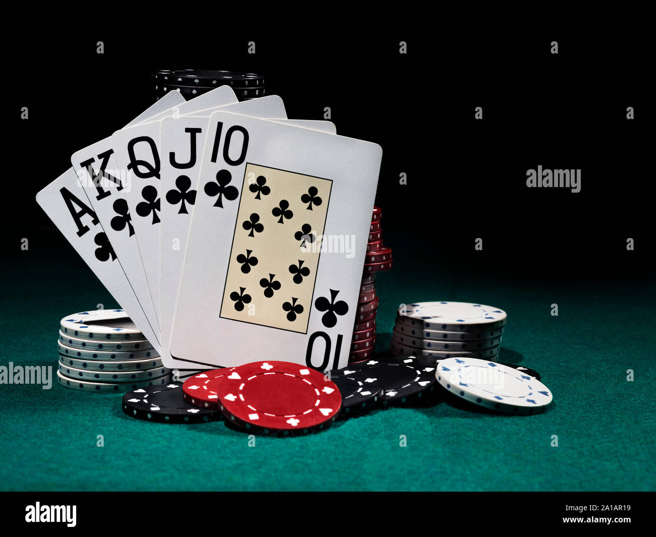 Royal Flush gestützt auf Chips Stapel auf grüne Abdeckung von Spielen. Schwarzen Hintergrund. Close-up. Stockfoto