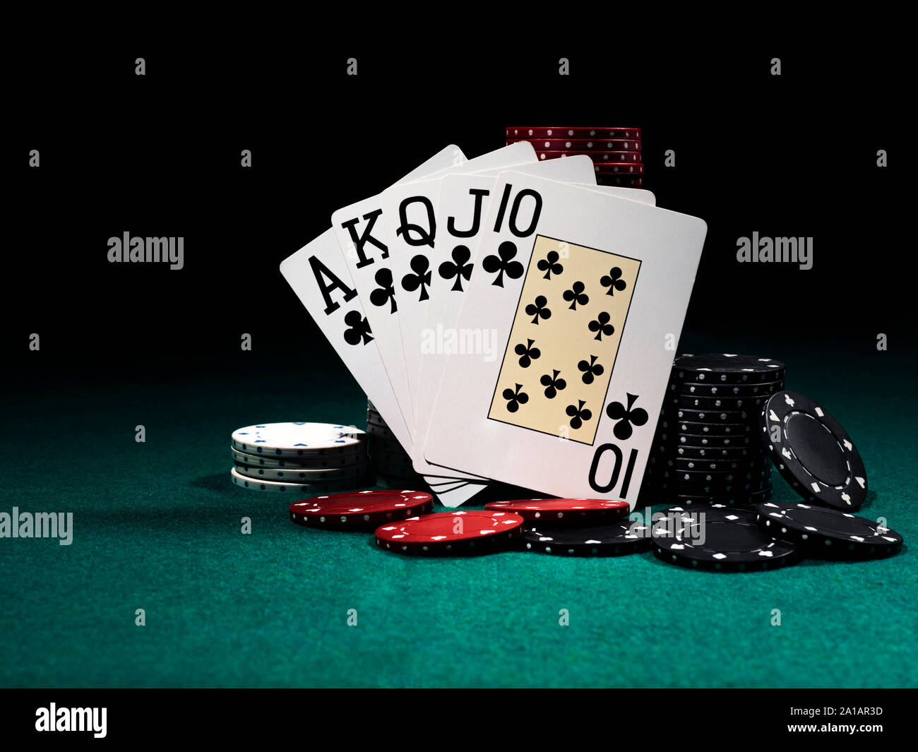 Royal Flush gestützt auf bunten Chips Stapel auf grüne Abdeckung von Spielen. Schwarzen Hintergrund. Close-up. Stockfoto
