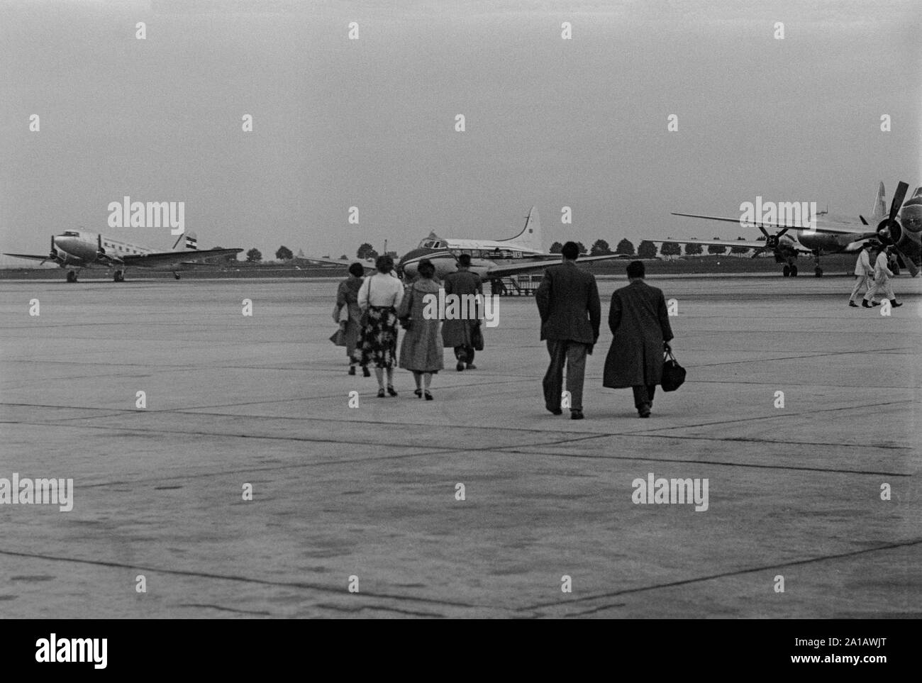 Die Mitte des zwanzigsten Jahrhunderts vintage Englisch schwarz-weiß Foto zeigt eine Gruppe von Passagieren gehen über Rollfeld des Flughafens auf den Status Warten auf De Havilland Dove Flugzeuge, Registrierung G-AKSK. Stockfoto