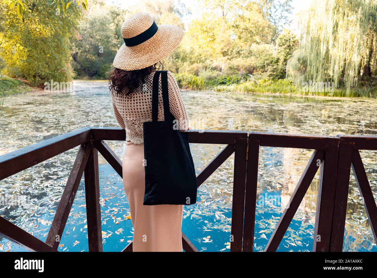 Frau in romantischen Kleidung und Stroh Hut mit schwarzen leere Tasche im Freien im Herbst oder Sommer Park in der Nähe von Teich. Für den leeren Raum. Kopieren Sie Platz. Eco Freund Stockfoto