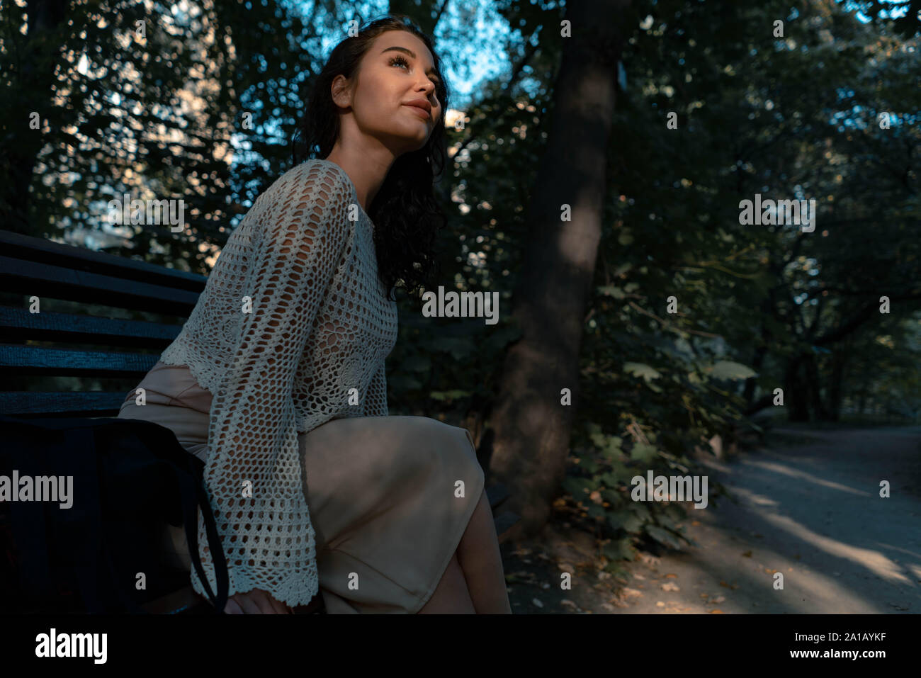 Frau in romantischen Kleidung und Strohhut im Freien im Herbst Park und genießen Sie gutes Wetter und Sonnenuntergang, beim Sitzen auf der Bank unter gotischen Bogen Stockfoto