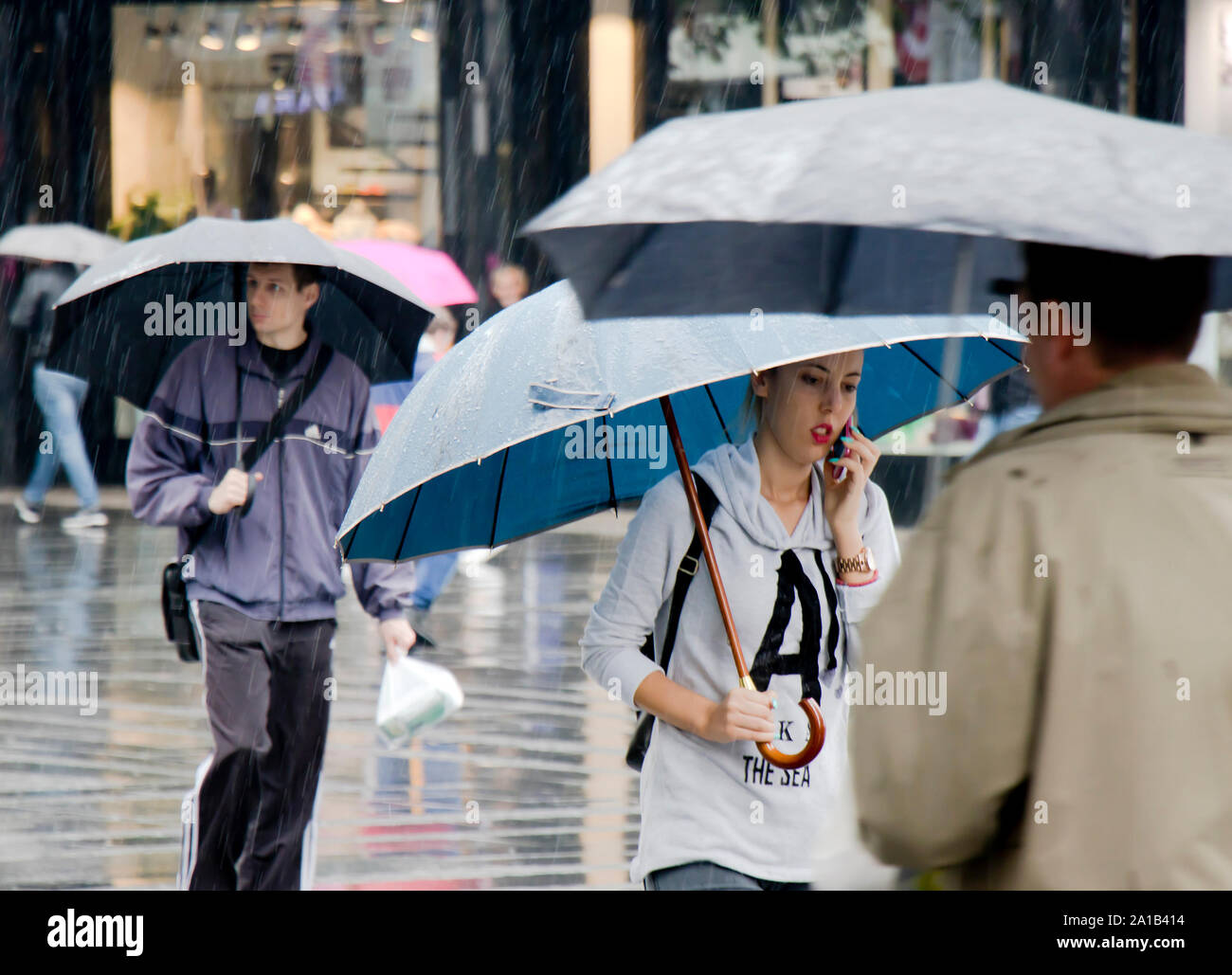 Belgrad, Serbien - September 24, 2018: Die junge Frau zu Fuß in Eile unter dem Dach beim Gespräch mit einem Mobiltelefon an einem regnerischen und Masse Ort Straße Stockfoto