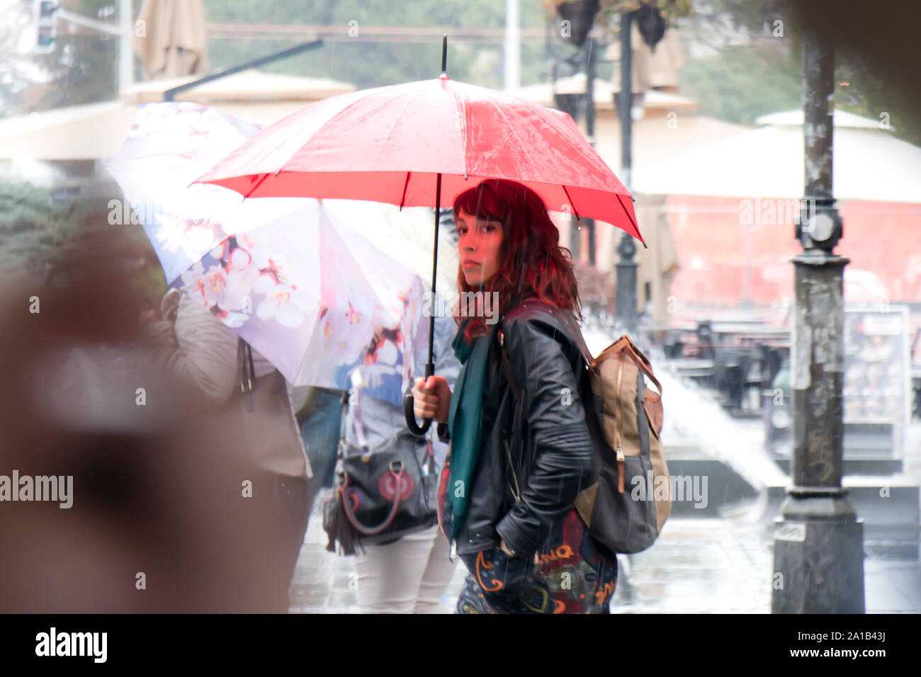 Belgrad, Serbien - September 24, 2018: Blurry junge Frau zu Fuß unter der rote Regenschirm an regnerischen und Masse Ort Straße Stockfoto