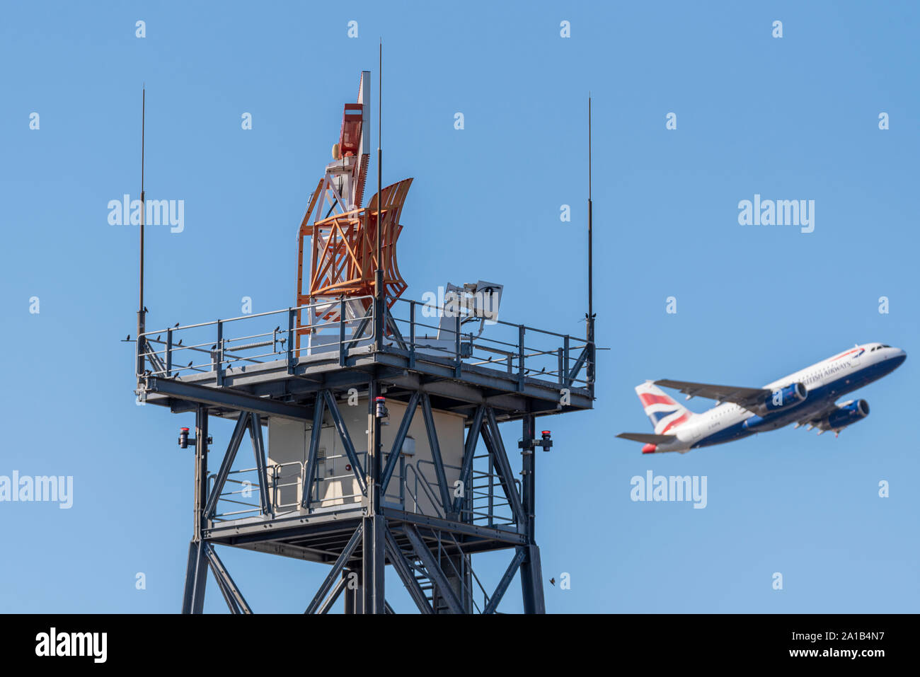 Eine Radarantenne am Flughafen London Heathrow in Betrieb. Kontrollierter Luftraum. British Airways Flugzeug startet. Vögel auf Struktur Stockfoto