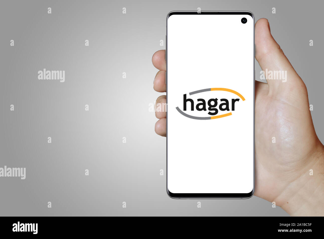Ein Mann hält ein Smartphone mit dem Logo der Firma Hagar Island an der Nasdaq gelistet. Grauen Farbverlauf im Hintergrund. Credit: PIXDUCE Stockfoto