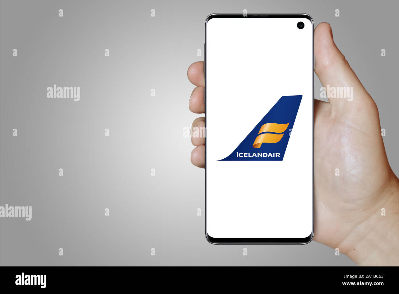 Ein Mann hält ein Smartphone mit dem Logo der Firma Island Icelandair Gruppe an der Nasdaq gelistet. Grauen Farbverlauf im Hintergrund. Credit: PIXDUCE Stockfoto
