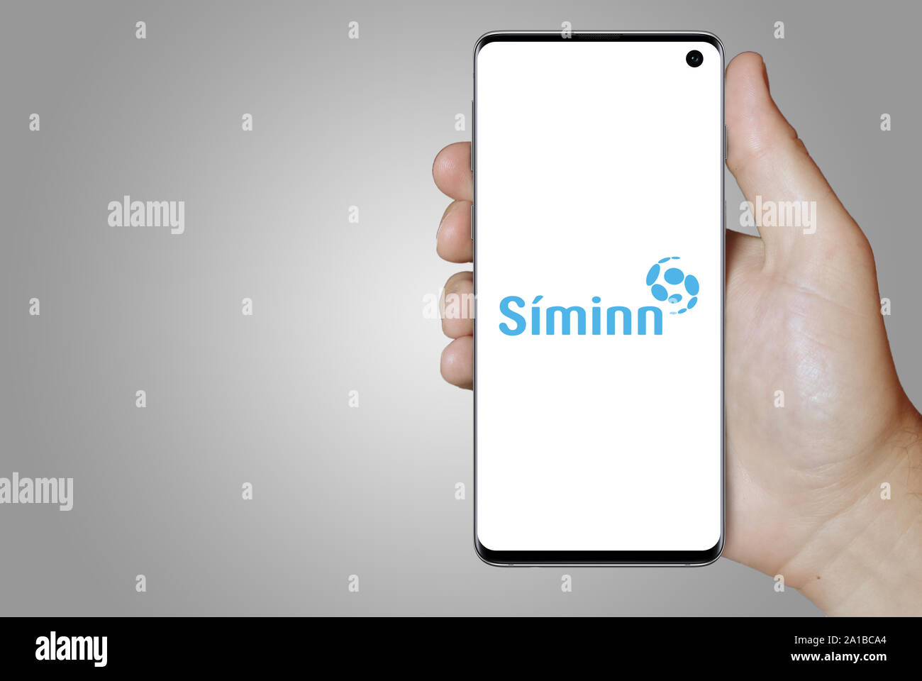 Ein Mann hält ein Smartphone mit dem Logo der Firma Síminn Island an der Nasdaq gelistet. Grauen Farbverlauf im Hintergrund. Credit: PIXDUCE Stockfoto