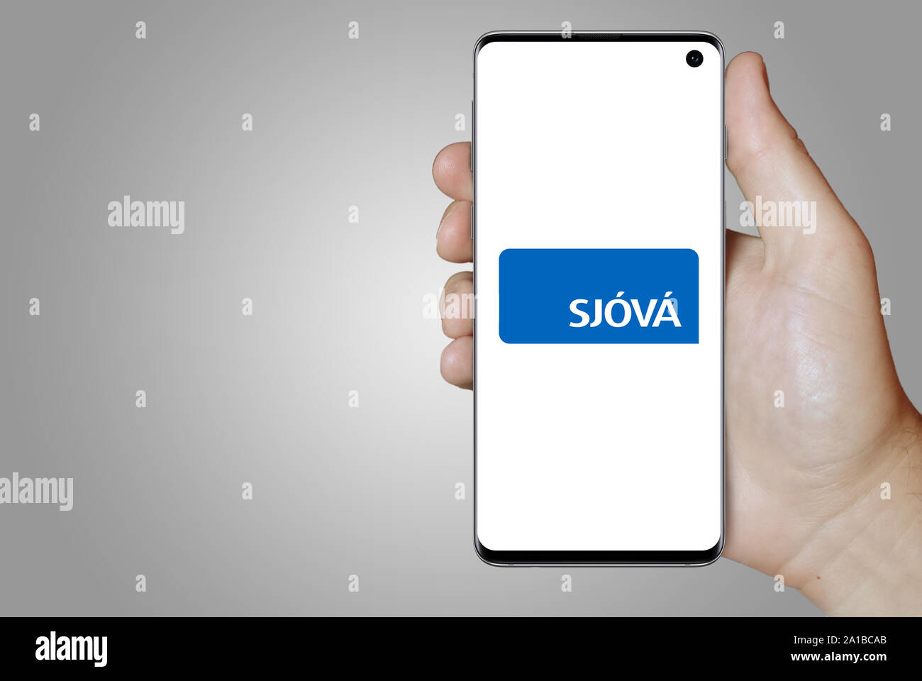 Ein Mann hält ein Smartphone mit dem Logo der Firma Sjóvá - Almennar tryggingar Island an der Nasdaq gelistet. Grauen Farbverlauf Hintergrund. Credit: PIXDUCE Stockfoto