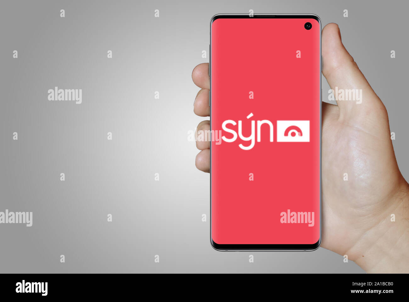 Ein Mann hält ein Smartphone mit dem Logo der Firma Sýn Island an der Nasdaq gelistet. Grauen Farbverlauf im Hintergrund. Credit: PIXDUCE Stockfoto
