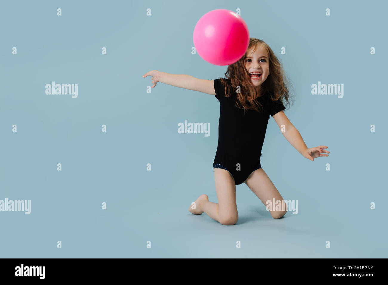 Kleines Mädchen in einem schwarzen Body mit rosa Gymnastikball über blauer Hintergrund Stockfoto
