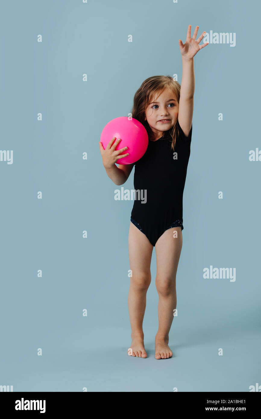 Kleines Mädchen in einem schwarzen Body mit rosa Gymnastikball über blauer Hintergrund Stockfoto